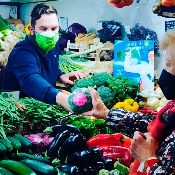 Un tendero ofrece una pieza de brócoli a una mujer en un mercado de hortalizas